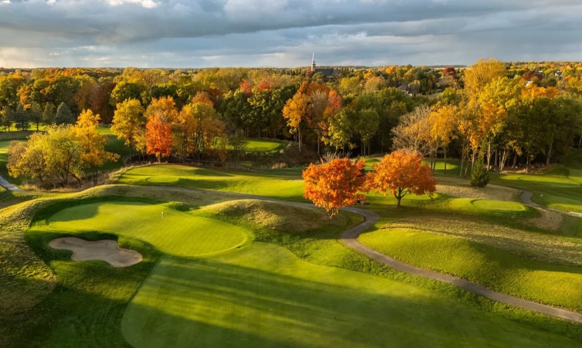 Aerial of the 1st green at The Fortress with the fairway sweeping toward the Frankenmuth steeple in autumn